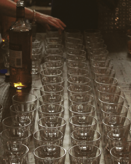 rows of glasses lined up with whiskey bottle