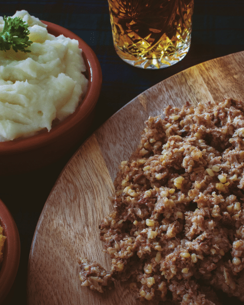 haggis served on wooden platter with mashed potatoes and whiskey in a glass